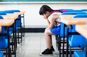 A little girl sitting in front of some desks