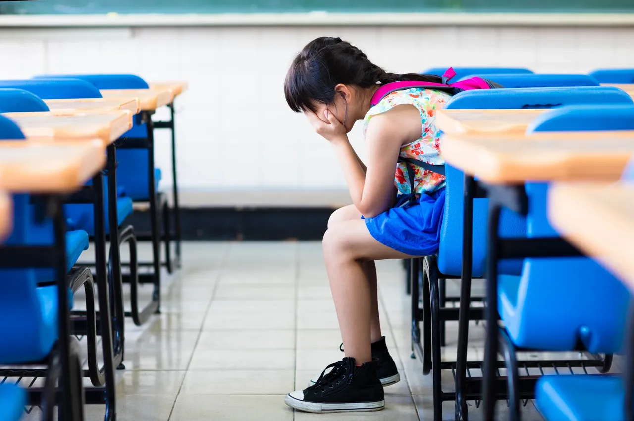 A little girl sitting in front of some desks
